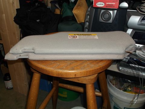 1999 Mercury Grand Marquis - A light gray sun visor is folded and resting on a wooden stool. A yellow warning sticker is visible on the top visor.