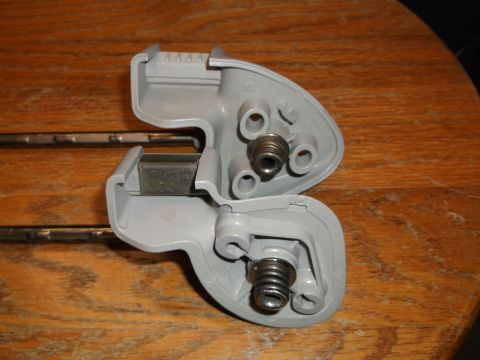 1999 Mercury Grand Marquis - Two gray plastic visor clips with metal rods are shown against a wooden background. Each clip has a spring-loaded mechanism visible.