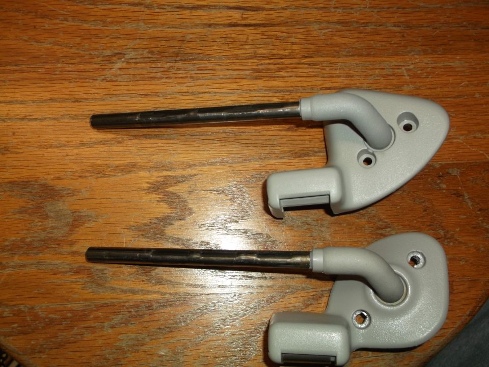 Two gray car sun visor brackets with metal rods on a wooden surface.