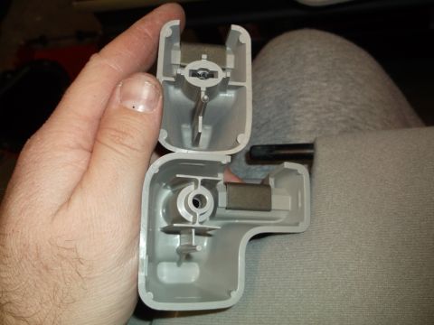 1999 Mercury Grand Marquis - A person's hand holds two disassembled gray plastic interior trim pieces, possibly for a sun visor, against a gray fabric background.