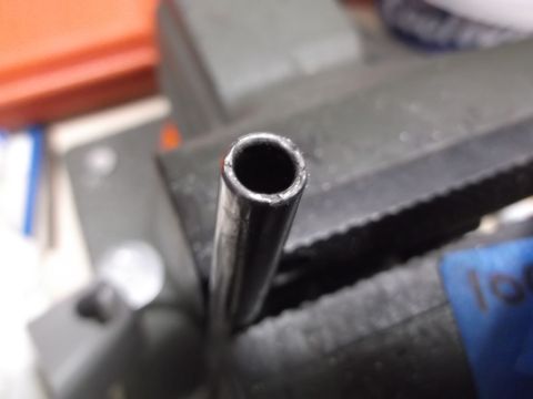 1999 Mercury Grand Marquis - Close-up view of the end of a metal tube held in a vise. The tube has a rough, cut edge and appears to be part of a mechanical assembly.