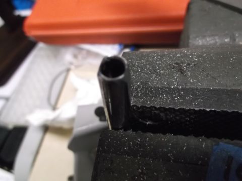 1999 Mercury Grand Marquis - A close-up shot shows the end of a black metal tube held in a black vise. In the background, an orange object is visible.