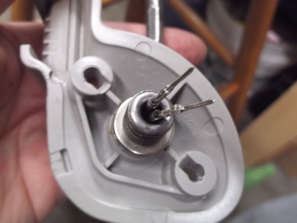 Close-up of a gray plastic vehicle part with two metal pins and a threaded connector.