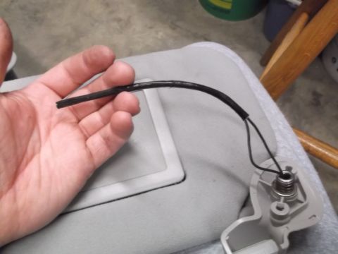 1999 Mercury Grand Marquis - A person's hand holds a black wire that appears to be detached from a spring-loaded mechanism on a light gray visor. The visor is likely fr…