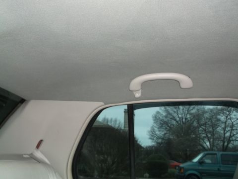 1999 Mercury Grand Marquis - Interior view of a car's headliner and grab handle, with a glimpse of the exterior through the rear window.