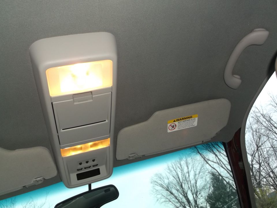 Car's overhead console with lights on, sun visor with warning label, and rearview mirror