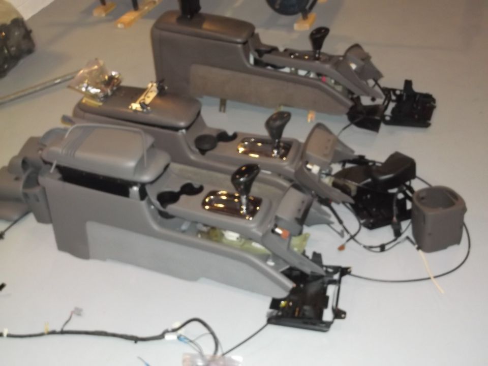 Two disassembled car center consoles with gear shifters and wiring harnesses on a floor