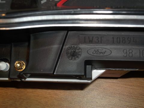 1999 Mercury Grand Marquis - A close-up view of a black plastic part from a vehicle's dashboard, featuring embossed text and a Ford logo. Visible text includes "1W3F-10…