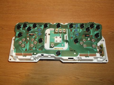 1999 Mercury Grand Marquis - The back of a green circuit board with numerous black and blue electrical components mounted on a white plastic housing. The circuit board…