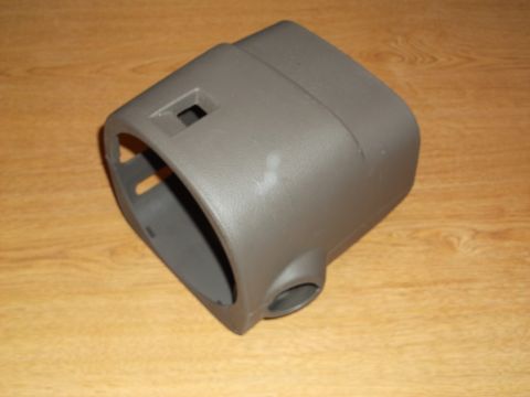 1999 Mercury Grand Marquis - A gray plastic steering column shroud is shown from a 3/4 front angle, resting on a wooden surface. The part has openings for the steering…