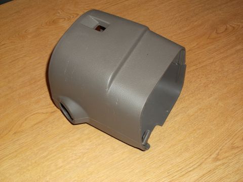 1999 Mercury Grand Marquis - A gray plastic steering column shroud is shown on a wooden surface. The part has openings for the steering column and potentially for switc…