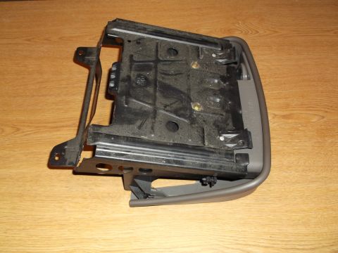 1999 Mercury Grand Marquis - This is a close-up, angled view of a dark gray plastic and metal automotive part, possibly a center console or seat component, resting on a…