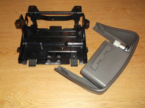 1999 Mercury Grand Marquis - Two disassembled parts of a car's interior console are shown on a wooden surface. The larger black plastic part is a bracket or frame, and…