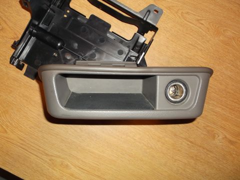 1999 Mercury Grand Marquis - A gray ashtray and cigarette lighter assembly is shown in the foreground, with a black plastic mounting bracket behind it. The parts are re…