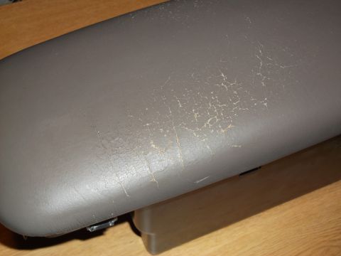 1999 Mercury Grand Marquis - The image shows a close-up of a cracked and peeling gray leather armrest, likely from a car interior. The surface shows significant wear an…