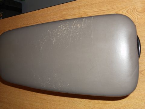 1999 Mercury Grand Marquis - A gray, padded armrest lid with visible scuffs and scratches is shown resting on a wooden surface. The lid appears to be from a vehicle's c…