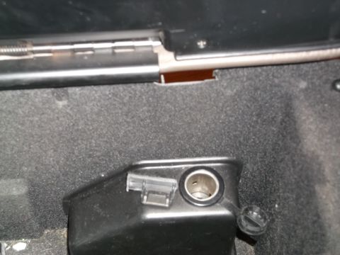1999 Mercury Grand Marquis - A close-up view of a black plastic housing containing a 12V power outlet, likely in a vehicle's interior. The outlet has a cap attached by…