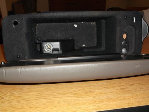 1999 Mercury Grand Marquis - The interior of a vehicle's center console storage compartment is shown open, revealing a black felt-lined bin with a circular audio jack a…