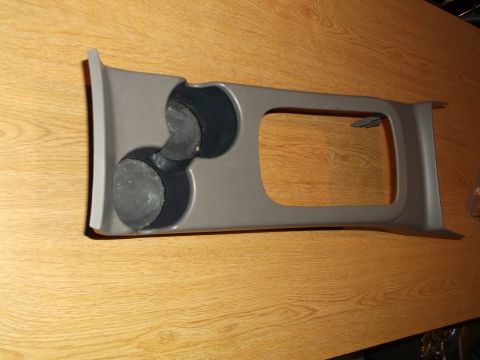 1999 Mercury Grand Marquis - A gray plastic center console cup holder assembly with two black rubber inserts is shown on a wooden surface.