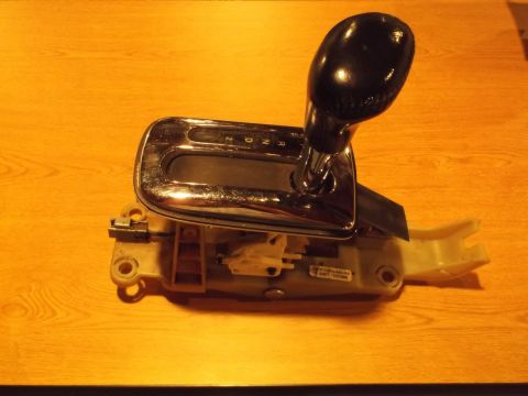 1999 Mercury Grand Marquis - A close-up view of a black automatic transmission shifter assembly with a chrome trim plate and a digital gear indicator showing P, R, N, D…