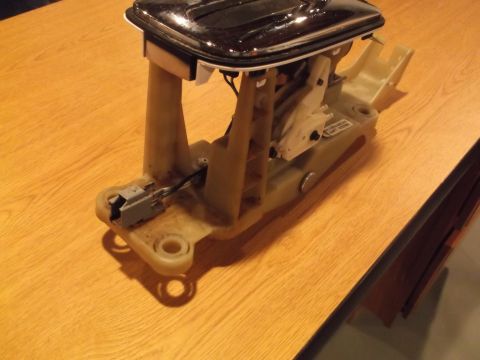 1999 Mercury Grand Marquis - A disassembled automatic transmission shifter assembly is shown on a wooden table. The assembly includes a chrome-trimmed shifter top, plas…
