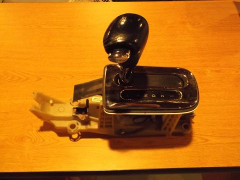 1999 Mercury Grand Marquis - A black automatic gear shifter assembly with a chrome trim surround is shown on a wooden surface. The gear indicator display shows N, D, an…