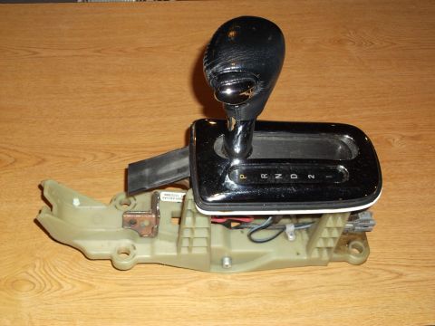 1999 Mercury Grand Marquis - A close-up view of a chrome-trimmed automatic transmission shifter assembly with a black leather shift knob. The shifter display shows P, R…