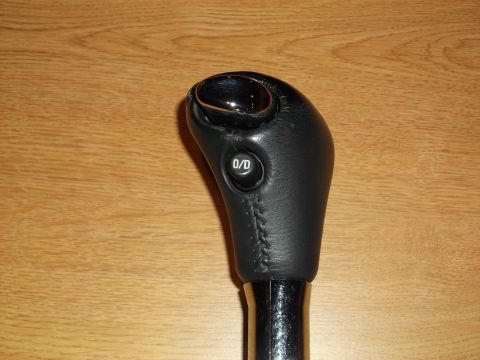 1999 Mercury Grand Marquis - A black leather-wrapped automatic gear shifter with a chrome button on top and a "O/D OFF" button on the side is shown against a wooden bac…