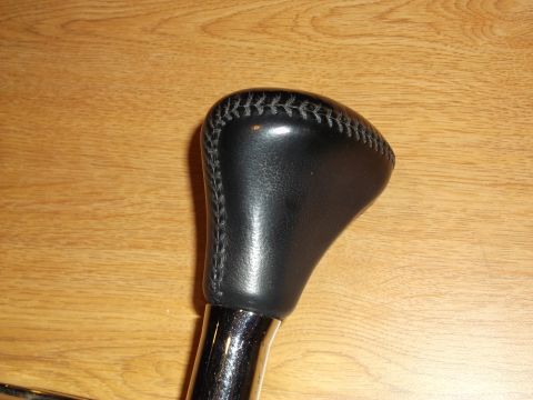 1999 Mercury Grand Marquis - A black leather-wrapped gear shift knob with visible stitching sits atop a chrome shaft. The knob is positioned against a light brown woode…