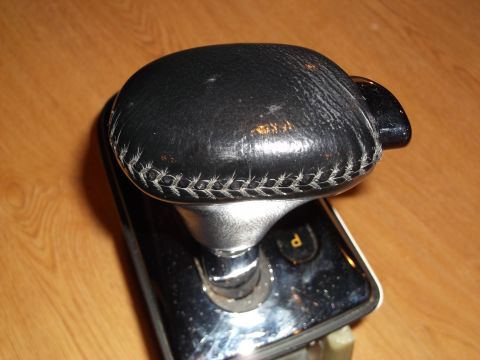 1999 Mercury Grand Marquis - A close-up, angled view of a black leather-wrapped gear shifter knob with white stitching, mounted on a chrome and black base. The base has…