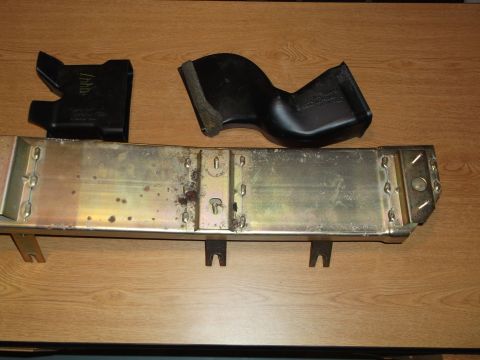 1999 Mercury Grand Marquis - Two black plastic ducting pieces and a long, rectangular, metallic bracket with some rust and dirt are laid out on a wooden surface.