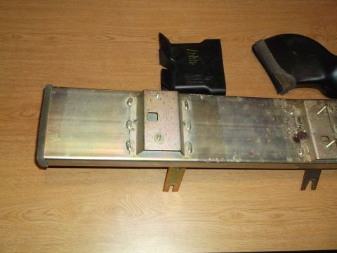 1999 Mercury Grand Marquis - A close-up, overhead shot shows a metal component with black plastic parts on a wooden surface. The metal part appears to be a structural e…