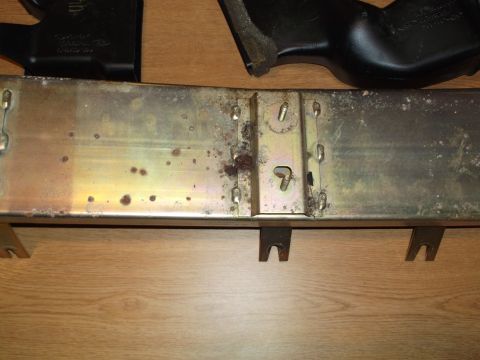 1999 Mercury Grand Marquis - A close-up view of a metal component with rust spots and some black plastic parts above it, resting on a wooden surface.