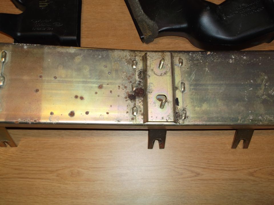 Metal component with rust and black plastic parts on a wooden surface.
