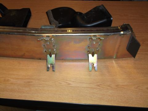 1999 Mercury Grand Marquis - A close-up view of a metal bracket assembly with two U-shaped metal tabs attached to the underside. Two black plastic air intake components…