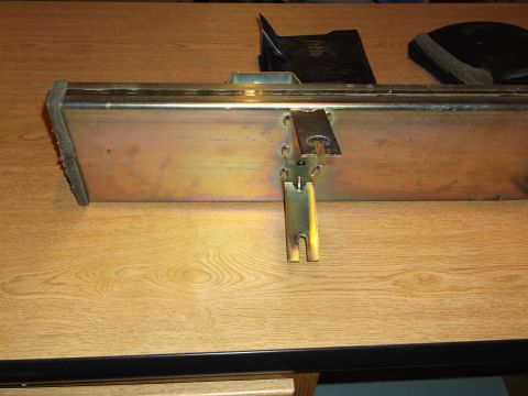 1999 Mercury Grand Marquis - A close-up view of a metal bumper or frame component with a latch mechanism attached, resting on a wooden surface.