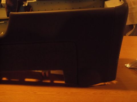1999 Mercury Grand Marquis - A dark-colored automotive part, possibly a bumper or side panel, is shown from a side angle resting on a wooden surface. The part has a rec…