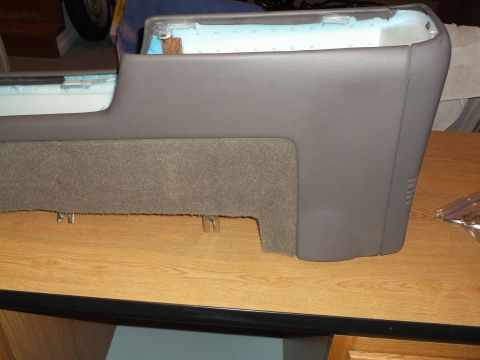 1999 Mercury Grand Marquis - A grey automotive center console section with carpeted lower trim is shown resting on a wooden surface. The interior foam padding is visibl…
