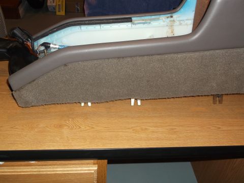 1999 Mercury Grand Marquis - A close-up view of a car's center console, upholstered in gray carpet and gray plastic, rests on a wooden surface. Several small white clip…