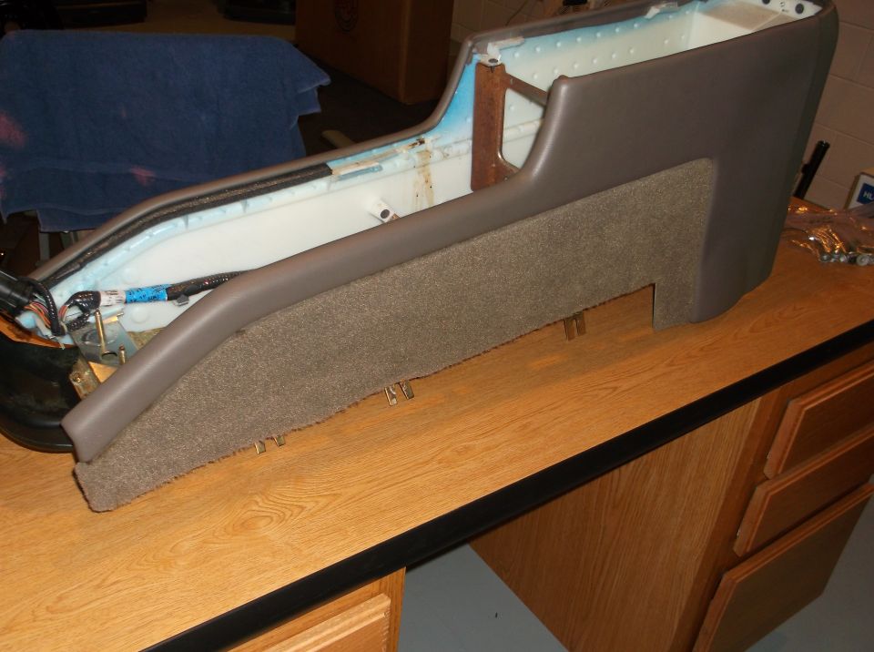 Disassembled car center console with brown upholstery and wiring on a wooden desk.