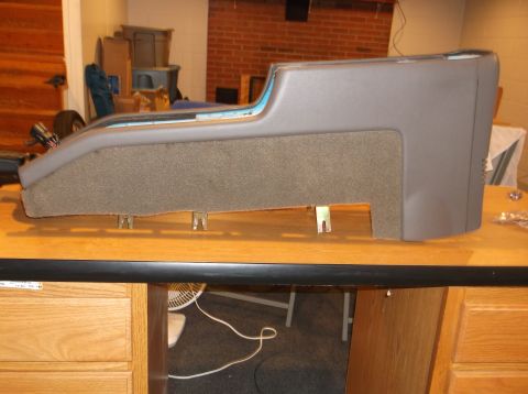 1999 Mercury Grand Marquis - A gray automotive center console with a textured fabric lower section is mounted on a wooden surface. Several metal brackets are visible un…