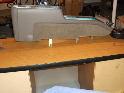 1999 Mercury Grand Marquis - A gray center console with a textured fabric insert sits on a wooden surface, likely a workbench. Metal mounting brackets are visible under…