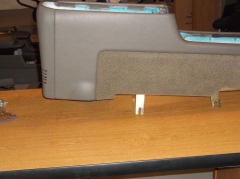1999 Mercury Grand Marquis - A close-up view of a gray center console part with a textured gray insert, resting on a wooden surface. Metal brackets are visible undernea…