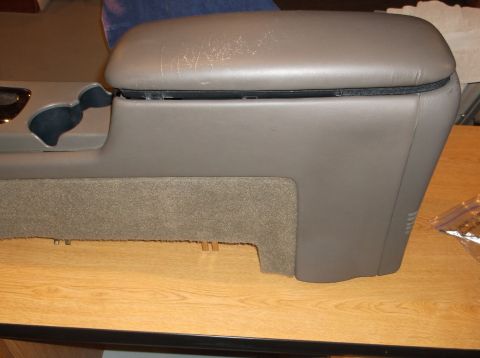 1999 Mercury Grand Marquis - A close-up, side view of a tan center console with a padded armrest and dual cup holders is shown on a wooden surface.