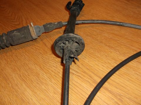 1999 Mercury Grand Marquis - A close-up view of a black shift cable with a rubber boot and a round, damaged plastic grommet is shown against a wooden background.