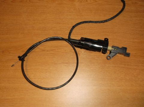 1999 Mercury Grand Marquis - A black throttle cable assembly with a black plastic housing is shown on a wooden surface. The cable is coiled to the left and extends to t…
