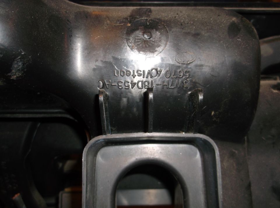 Black plastic automotive part with embossed text and Ford logo.