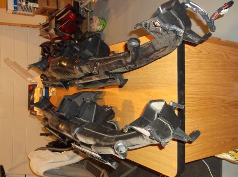 1999 Mercury Grand Marquis - Two black plastic automotive HVAC ducting assemblies are laid out on a wooden table. The upper assembly has wiring bundles attached to it.