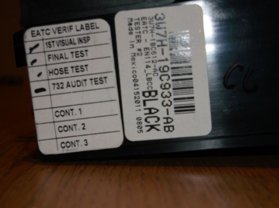Close-up of two labels on a black car part, one with inspection results and the other a barcode.