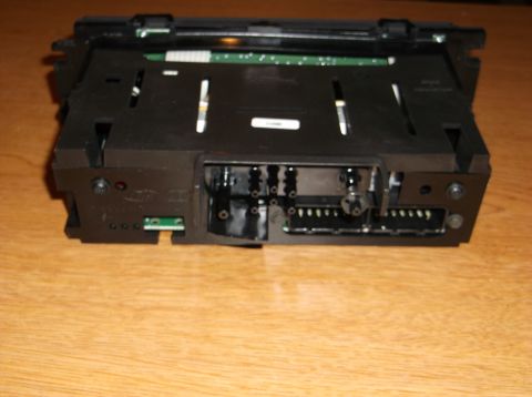 1999 Mercury Grand Marquis - The rear of a black car stereo unit is shown, mounted in a black plastic housing. The unit has multiple connectors and a circuit board visi…